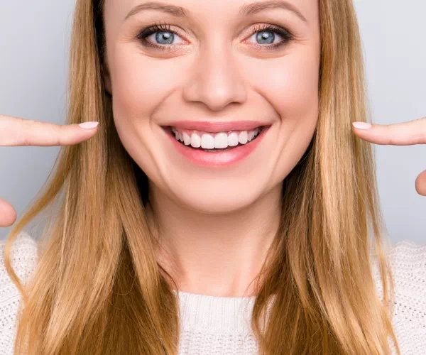 Uśmiechnięta kobieta wskazująca palcami swoje zęby